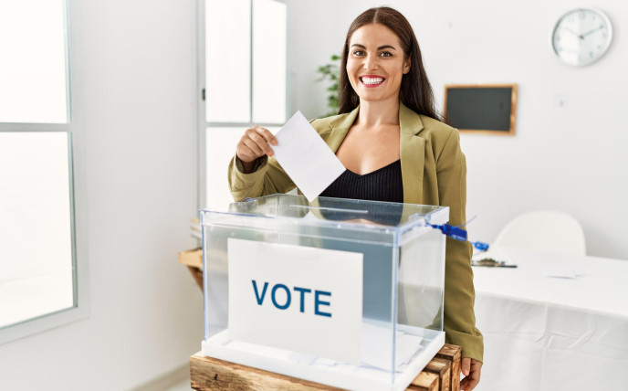 Young woman smiling and putting her vote into a ballot box