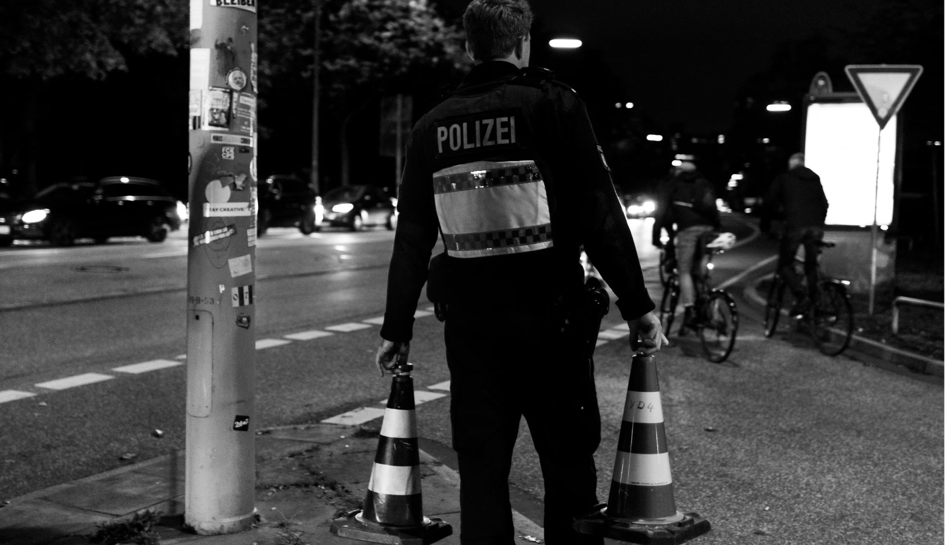 German police officer carrying two traffic cones onto a street