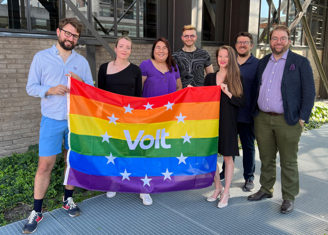 Candidates for Volt standing together holding up a Volt LGBTQIA+ flag