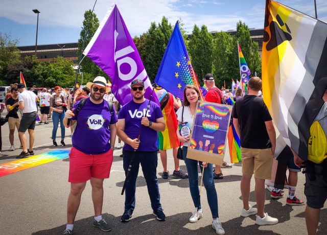 Philippe Schannes holding a Volt flag, Daniel Silva holding a EU/Pride flag and Aurélie Dap holding a poster with 