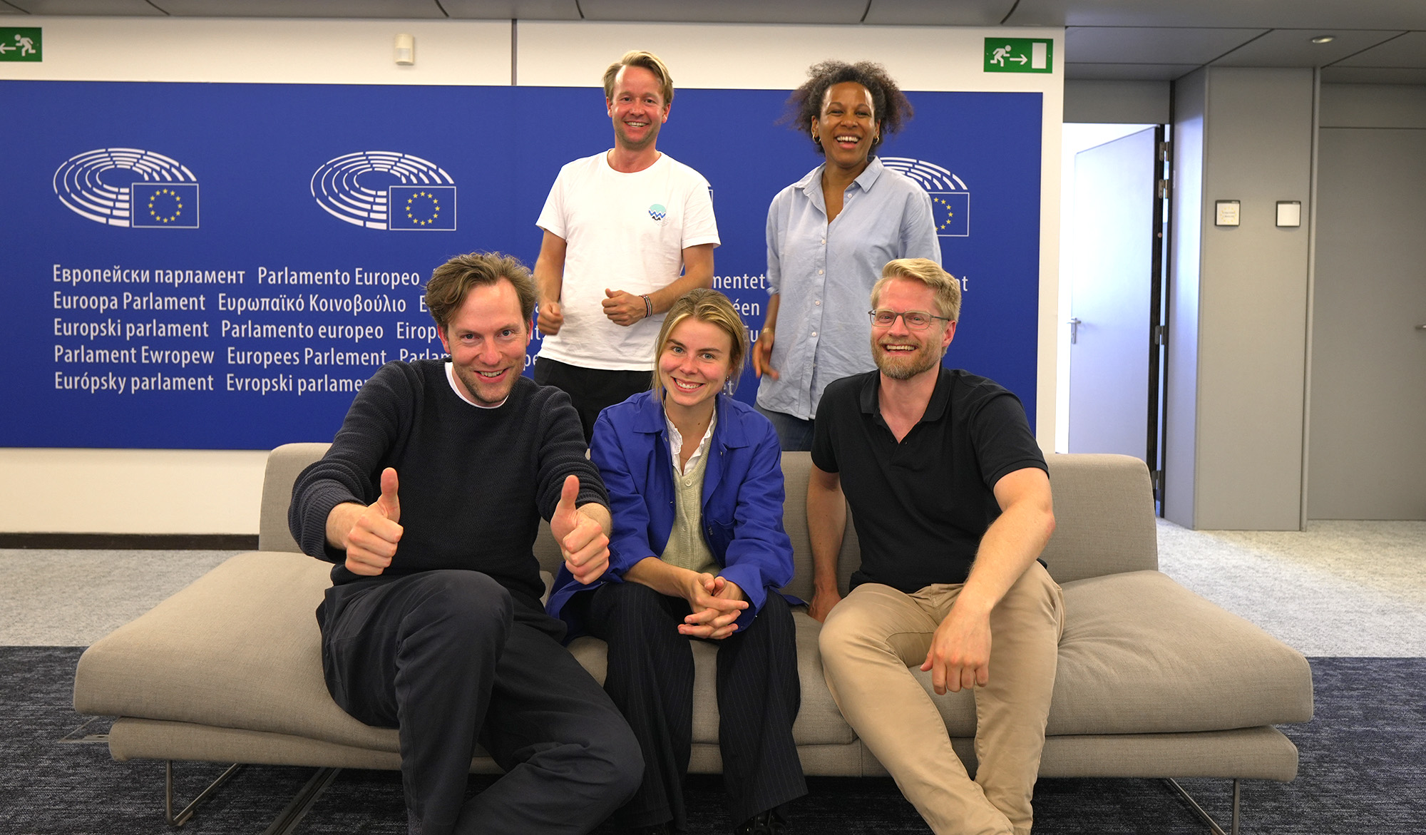 The 5 MEPs from Volt inside of the European parliament, three in front sitting on a couch, two standing behind them.