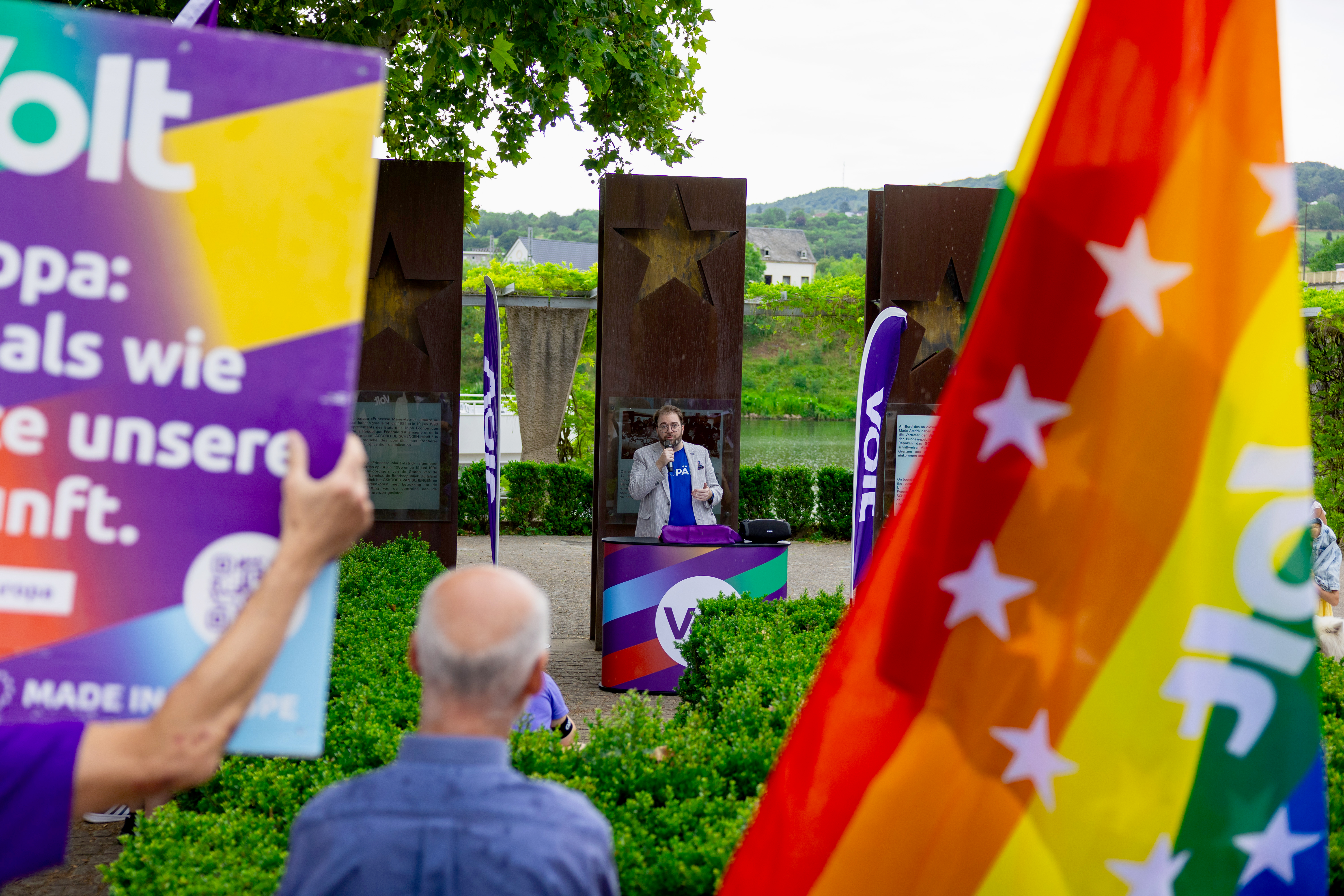 Philippe Schannes behind a podium giving a speech. In the foreground there are blurred Volt posters and flags