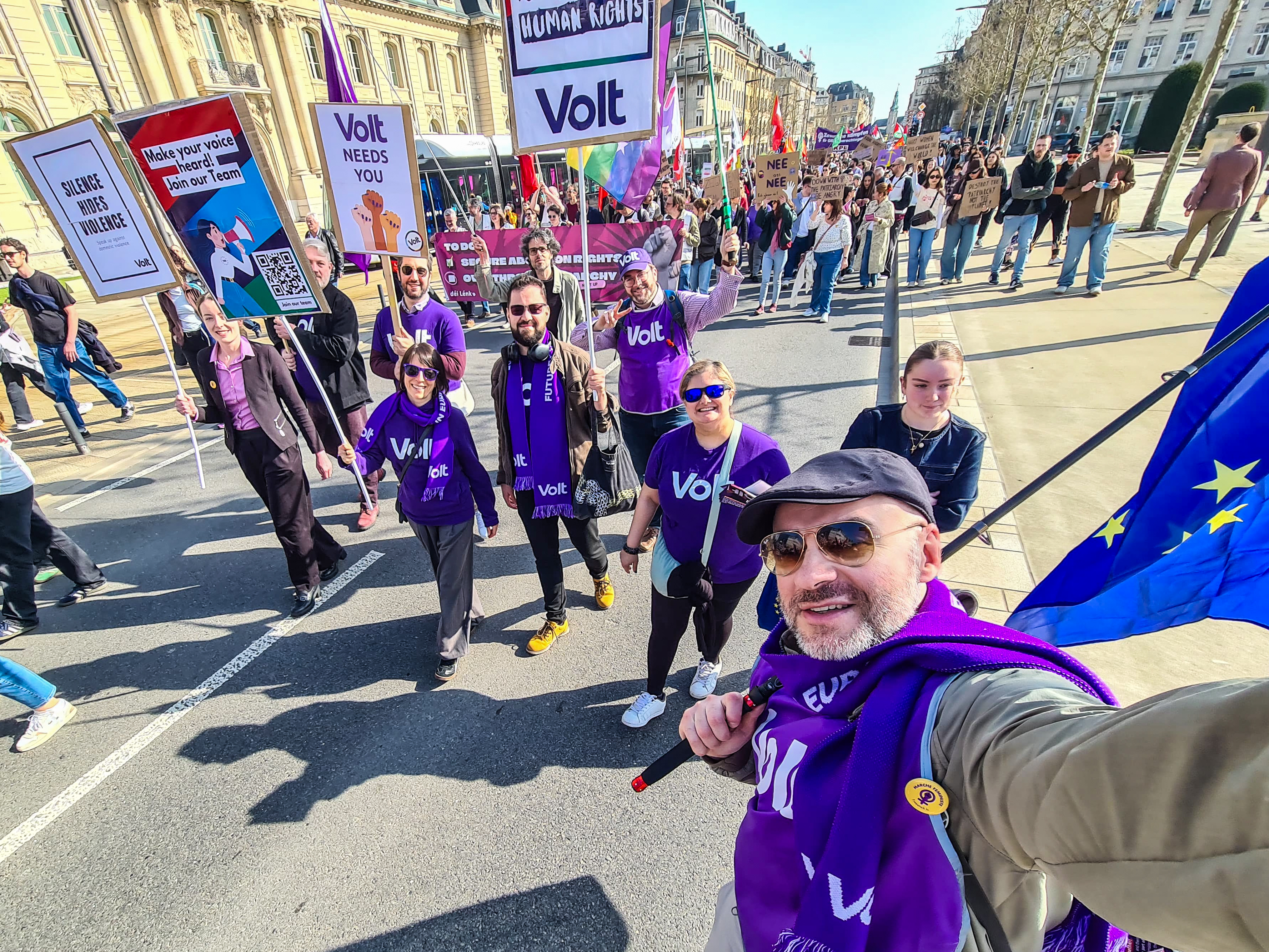 Volters going in the march (in the streets) with flags and posters. Lots of people in the background.